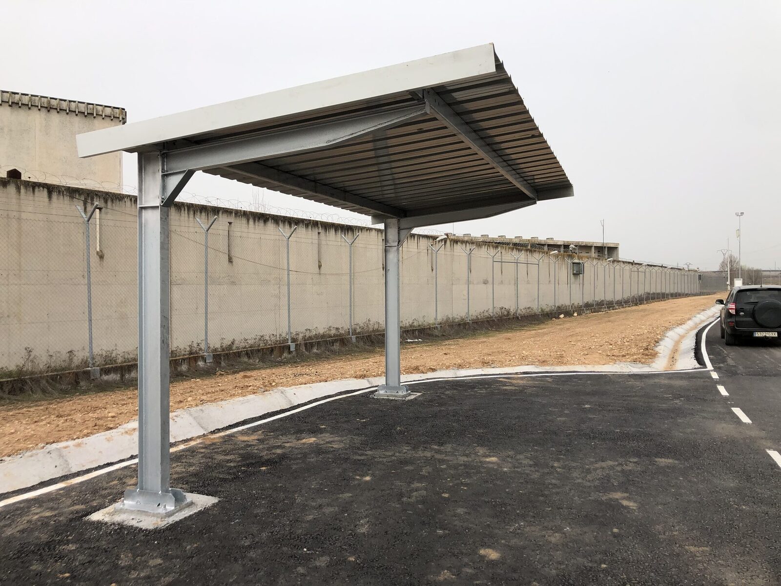 Sombraje de un solo poste junto a un muro, en un acceso rodado